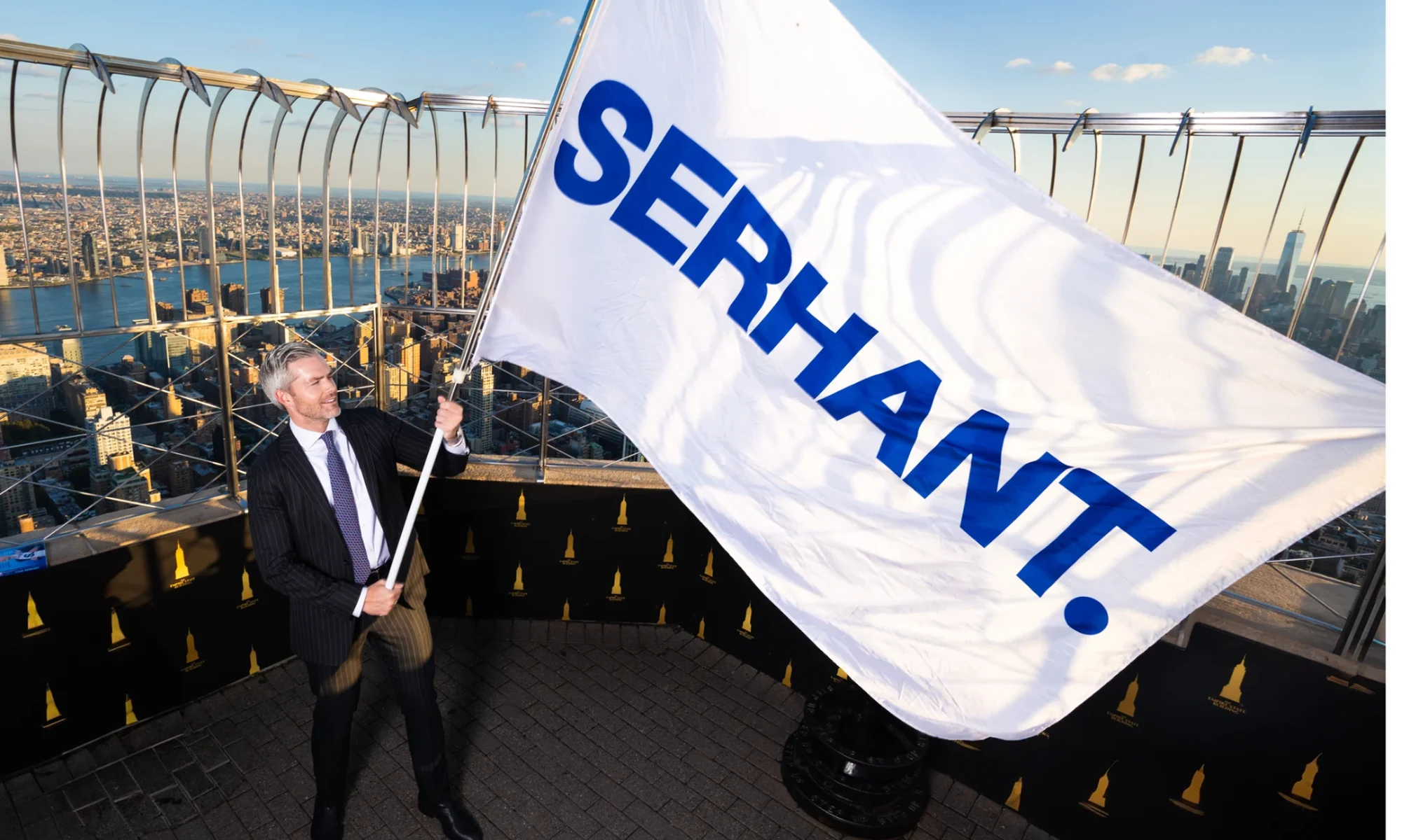 Ryan Serhant holding a SERHANT. flag above the Boston skyline